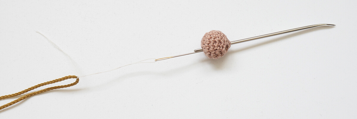 Instrucciones de elaboración del amuleto de perlas con forma de animalito: Cordón de hilo para las piernas a través de la cuenta de ganchillo